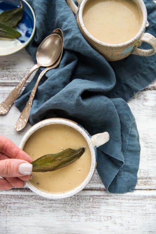 placing a fried sage leaf on top of a bowl of soup