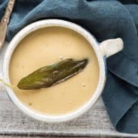 close up of bowl of parsnip and white bean soup with a fried sage leaf