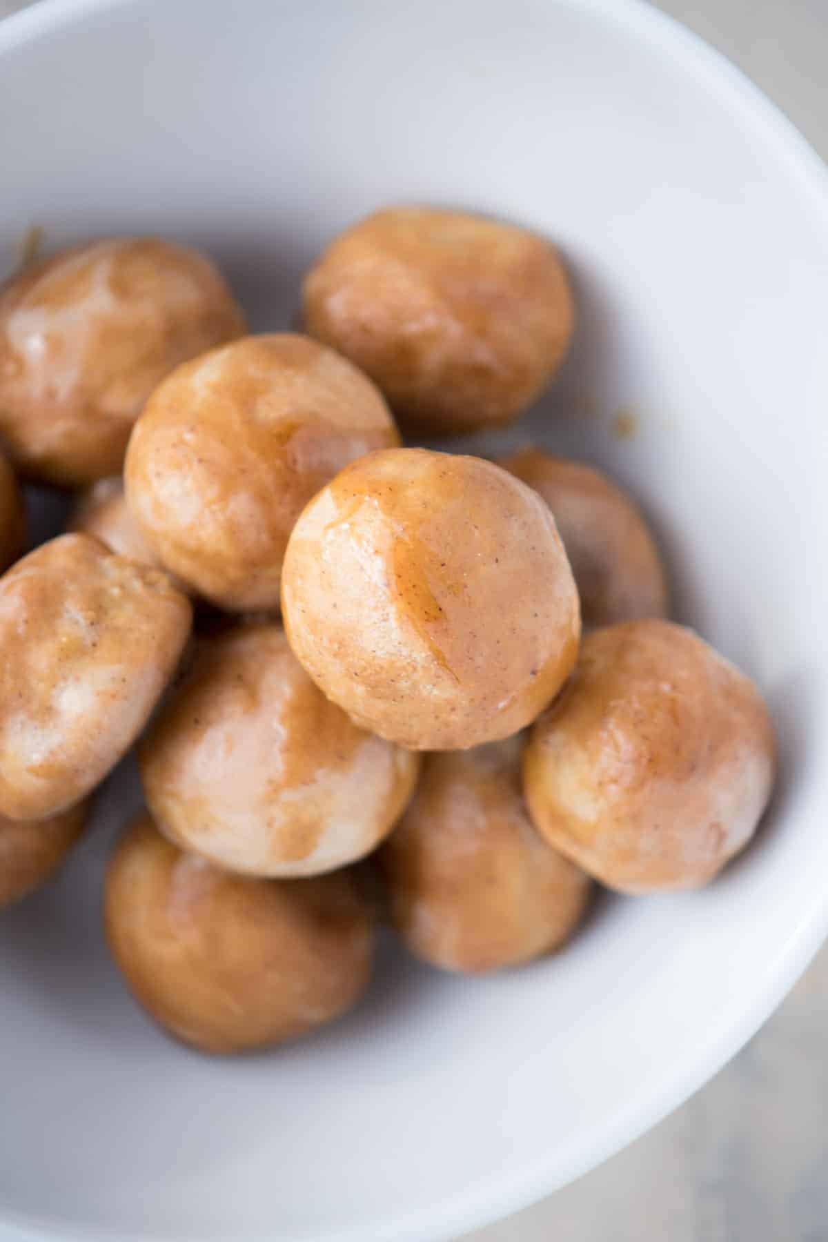 A white bowl of glazed gingerbread doughnut holes.