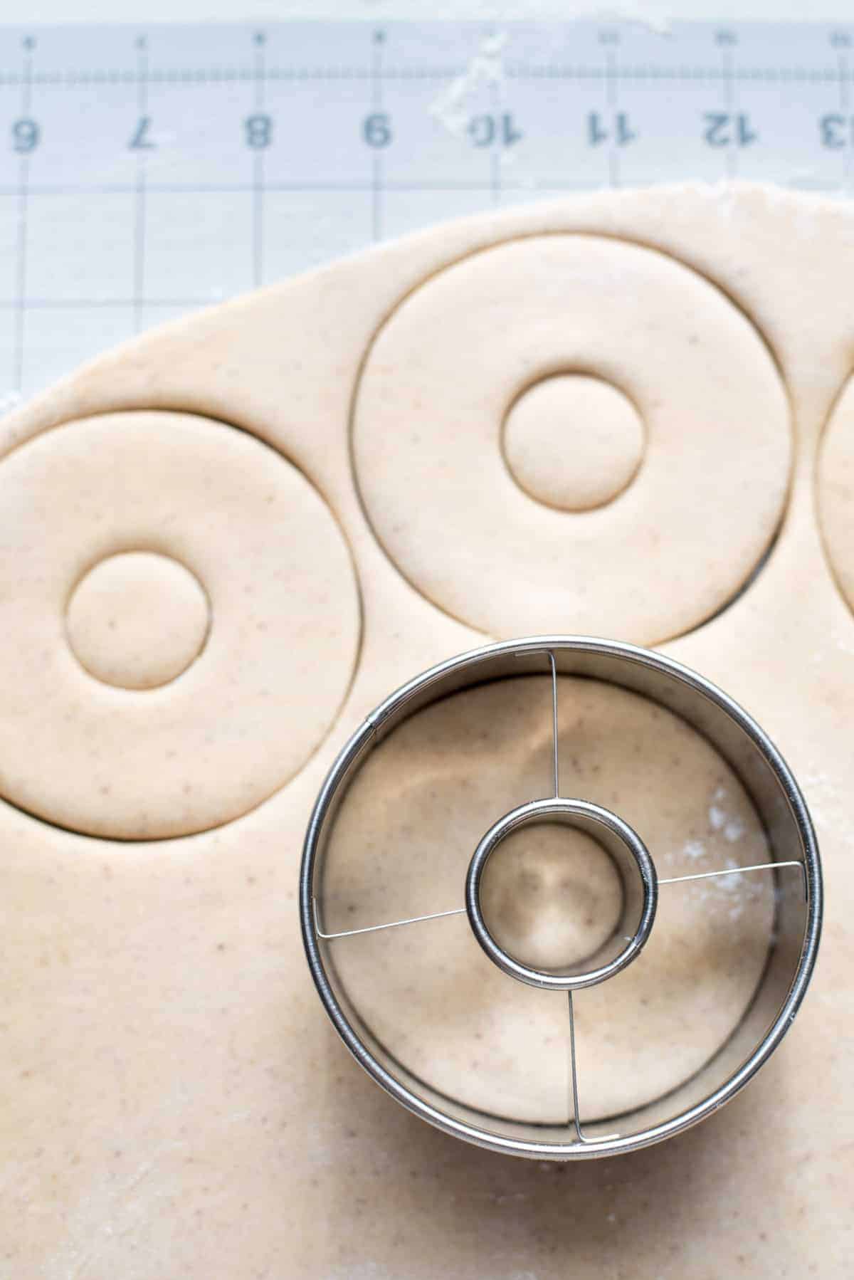 The gingerbread doughnut dough is sitting on top of graph paper and a cutter is being used to cut the doughnut shapes out. You can see 2 of the doughnuts cut from the dough already and another is being cut with the cutter here.