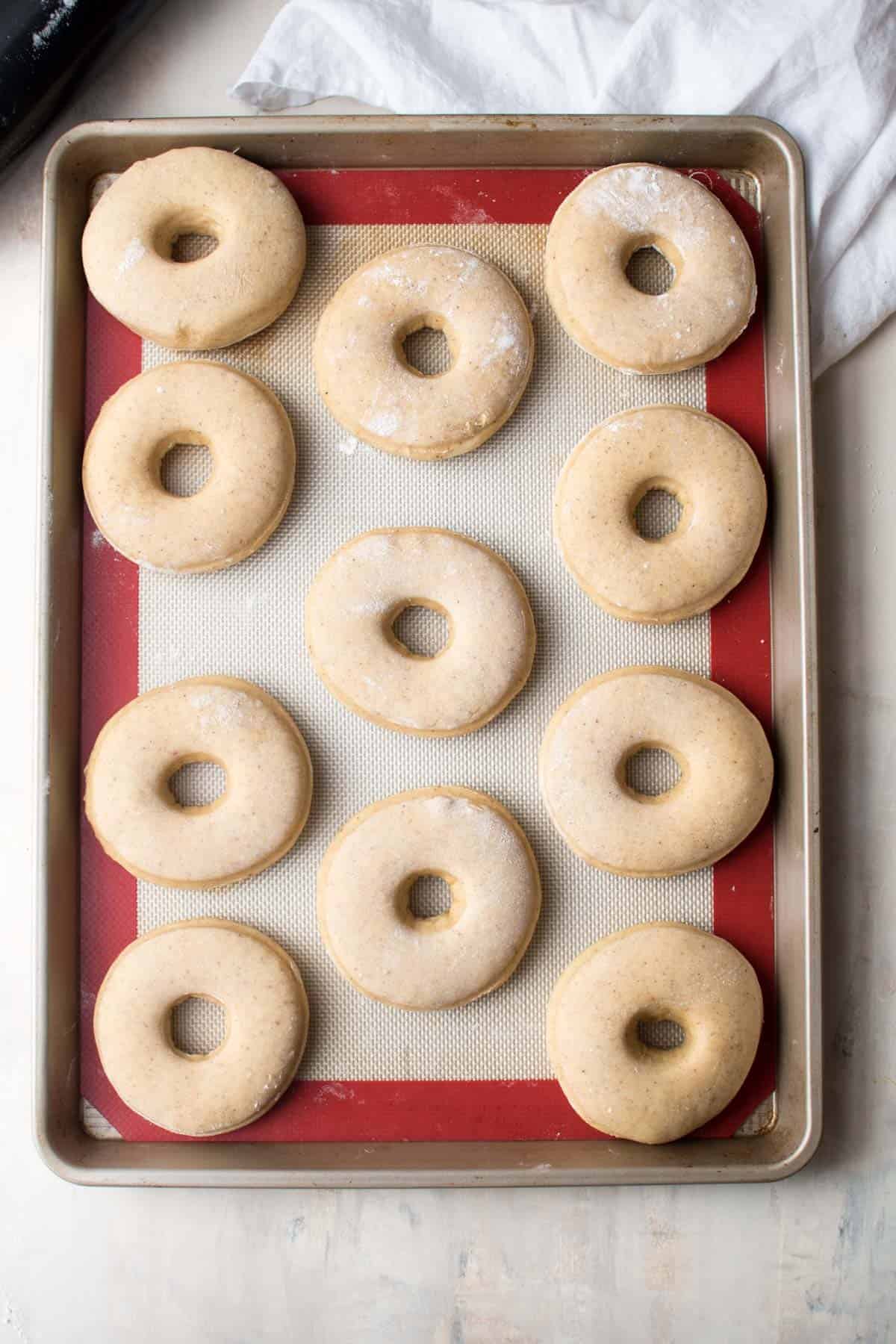 The doughnuts are on a silver and red baking tray, in an O shape with a hole in the middle, they dough has risen and the doughnuts look full and ready to be baked.