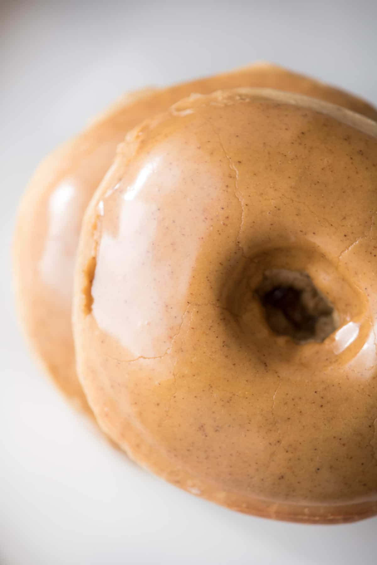 View from above of 2 gingerbread doughnuts stacked on top of each other on a white surface. The glaze on top is shiny.