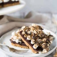 No Bake S'mores Bars are bringing everything good about summertime camping without the bug bites.  Crunchy graham cracker crust, creamy chocolate center and gooey toasted marshmallow topping.  Best of all, no oven needed. #smores #nobake #kidfriendlydesserts #camping #summerdesserts #usesforakitchentorch