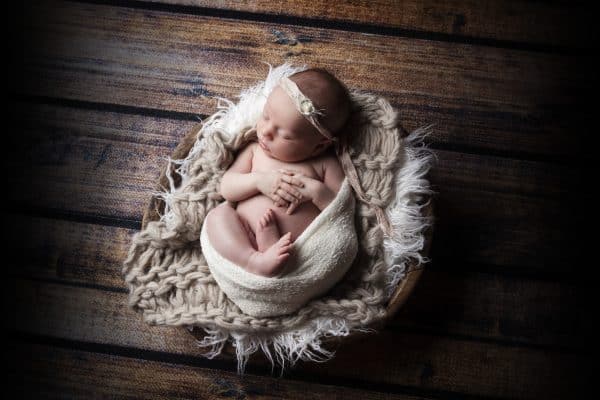 Newborn photo in wooden bowl with fur blanket.