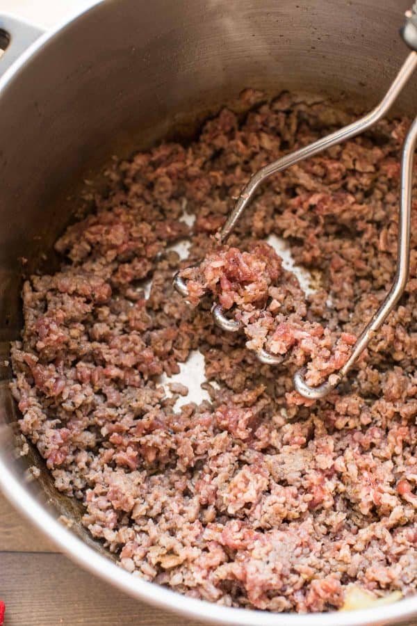 using a potato masher to finely saute sausage