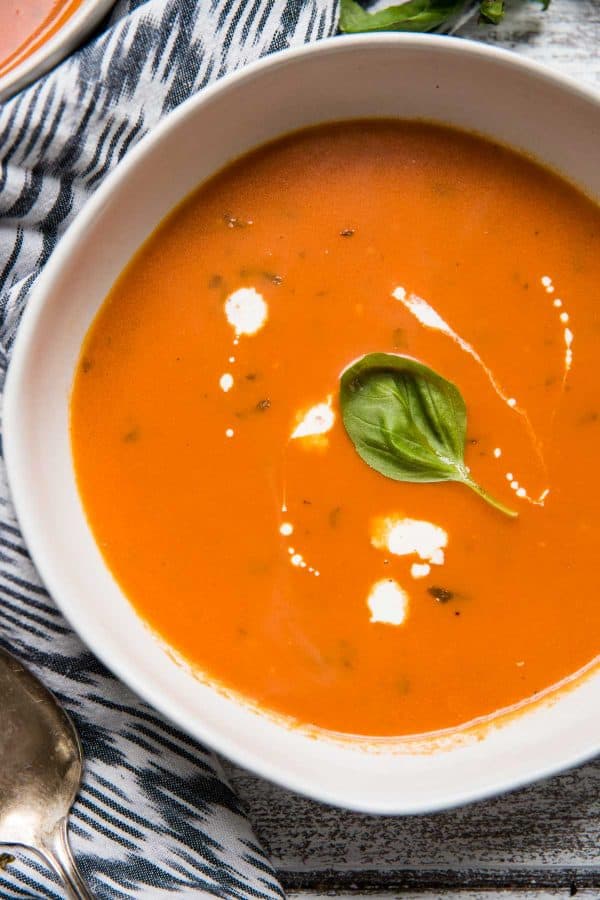 close up photo of tomato basil soup with streaks of heavy cream and a basil leaf on top