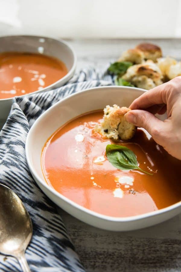 garlic knots being dipped into creamy tomato basil soup