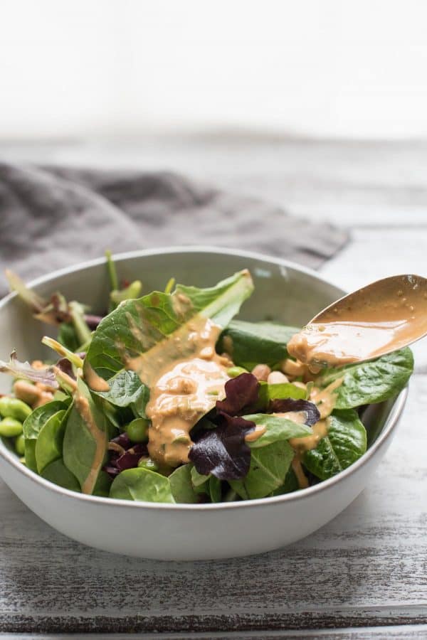 low calorie thai peanut dressing being spooned on top of a salad