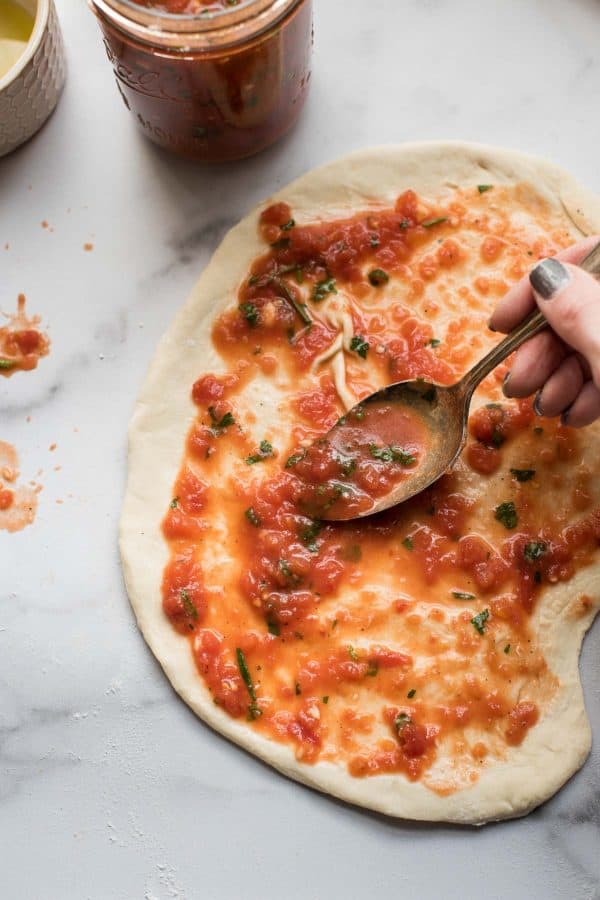 spreading homemade pizza sauce on dough