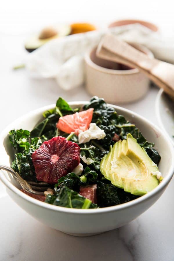 small bowl of kale citrus salad topped with thinly slice avocado