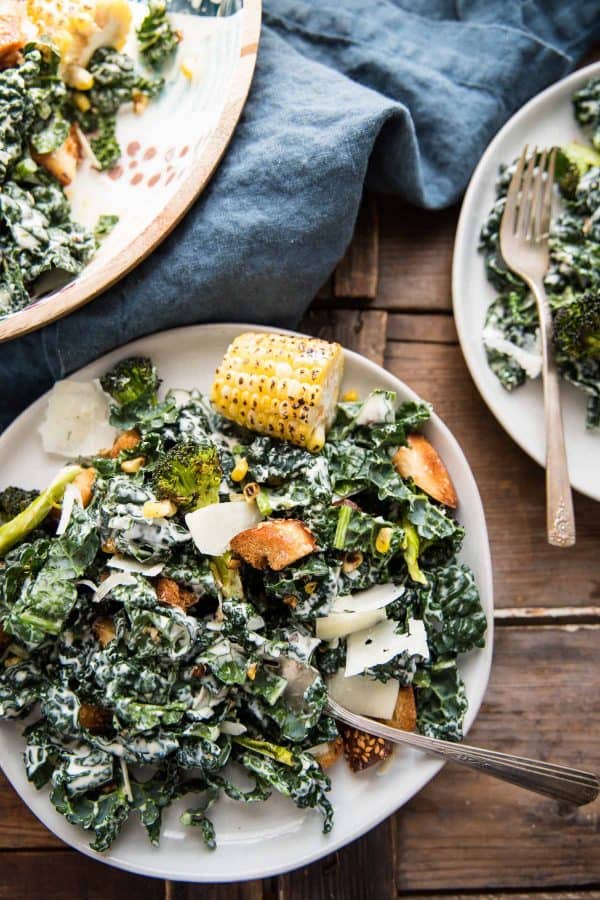 roasted broccoli and kale caesar salad in a bowl and plated on two plates