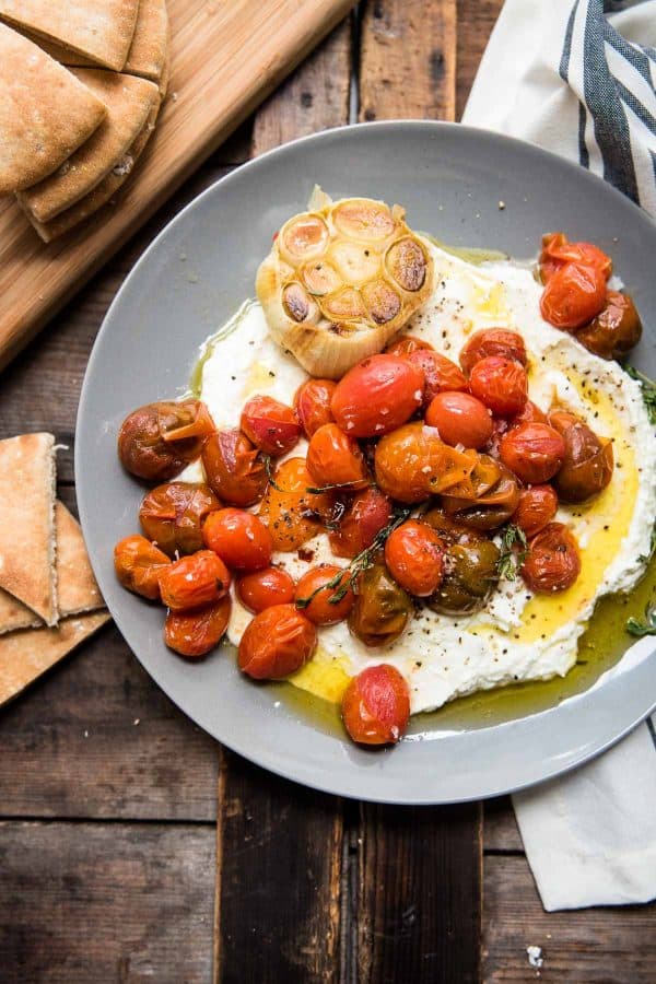 whipped feta topped with roasted garlic and blistered tomatoes on a grey serving plate