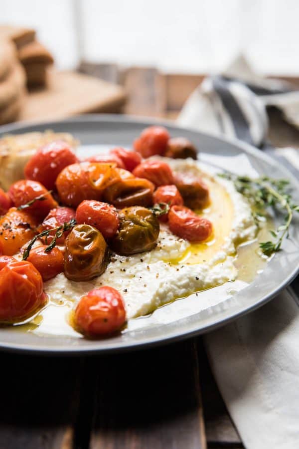 close up of blistered tomatoes and roasted garlic oil on top of creamy whipped feta