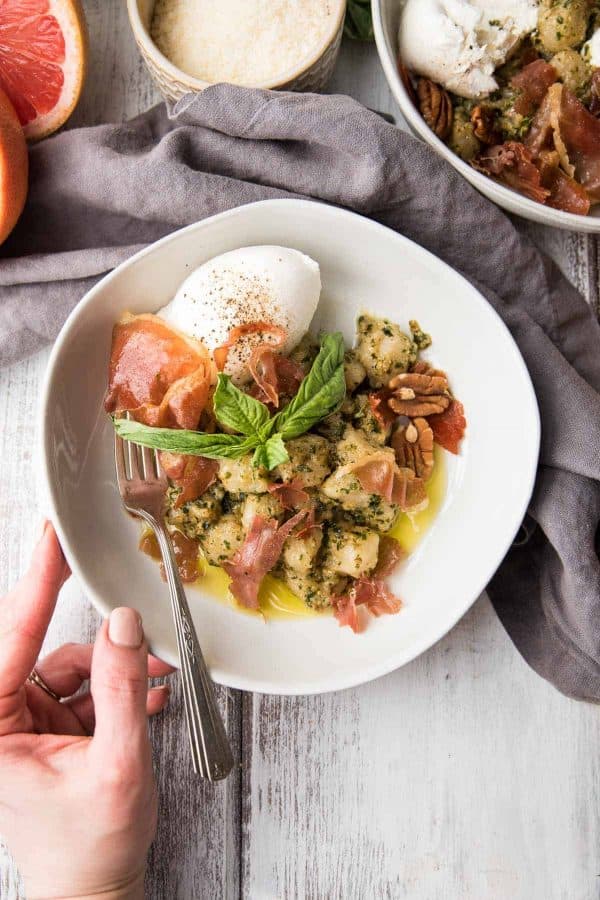 hand adjusting bowl of cauliflower gnocchi with pesto