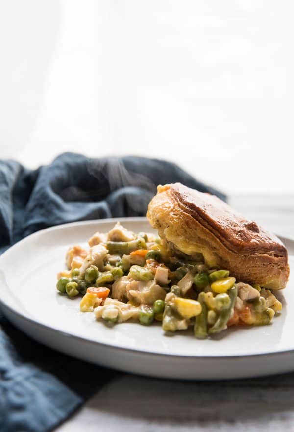 chicken pot pie steaming on a plate topped with a buttered biscuit