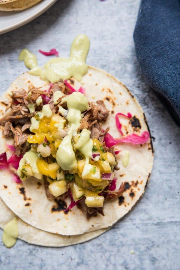 up close shot of avocado crema drizzled over pork carnitas tacos