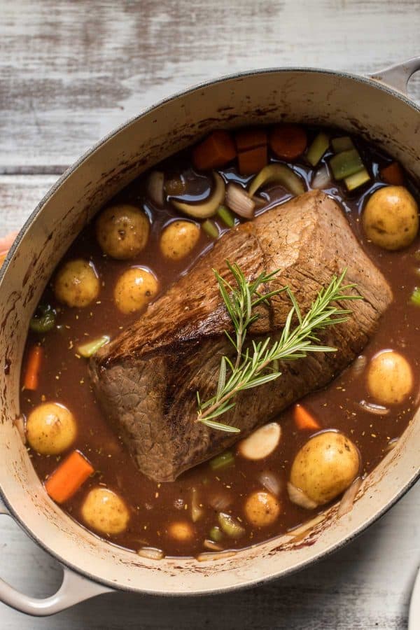 whole beef pot roast in dutch oven with vegetables and fresh herbs