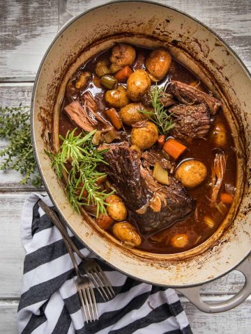 whole beef pot roast in dutch oven with vegetables and fresh herbs