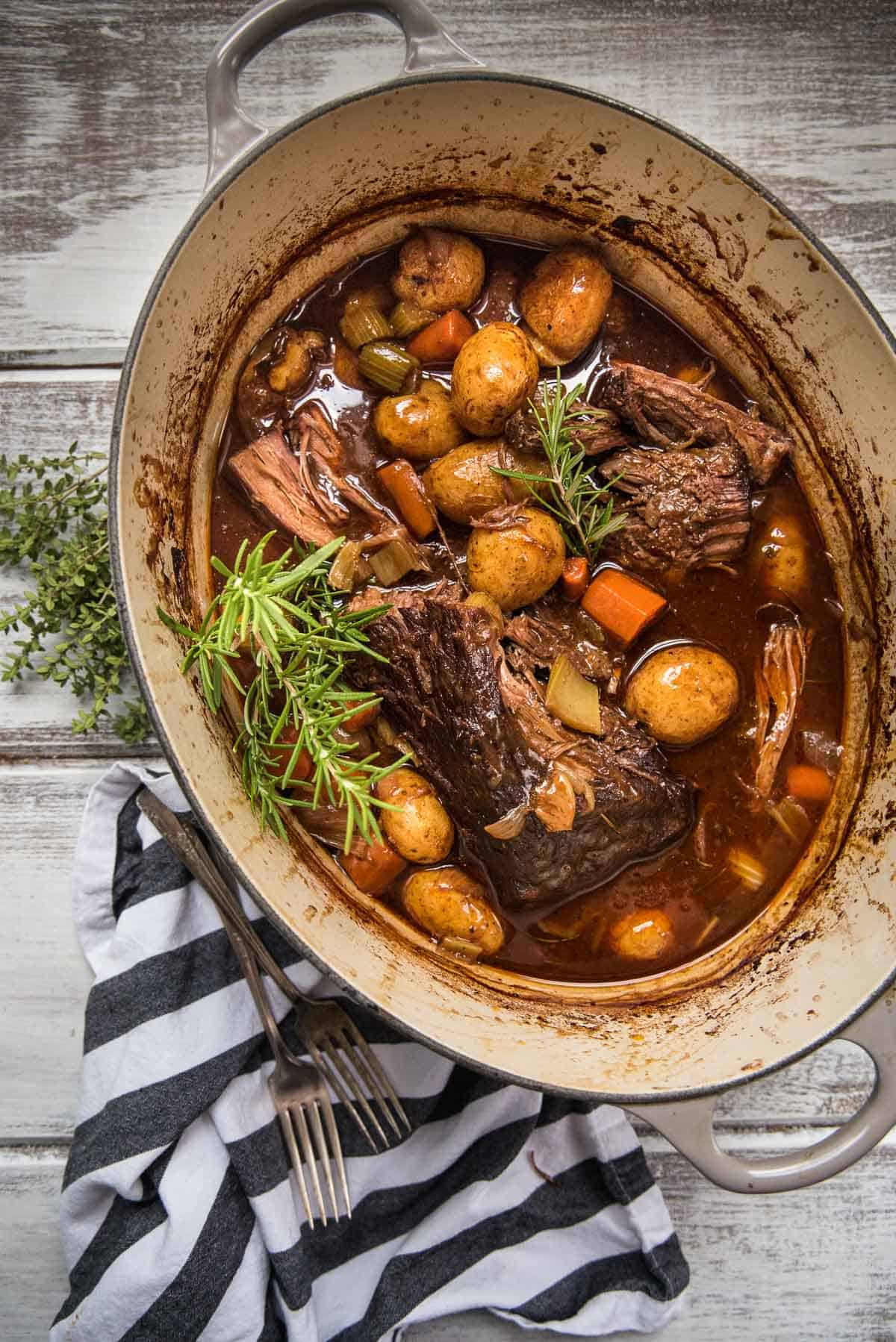 whole beef pot roast in dutch oven with vegetables and fresh herbs