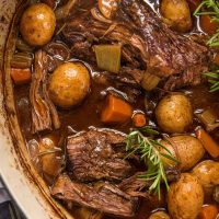 slightly shredded roast in dutch oven with vegetables and fresh herbs
