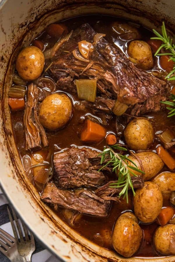 slightly shredded beef pot roast in dutch oven with vegetables and fresh herbs