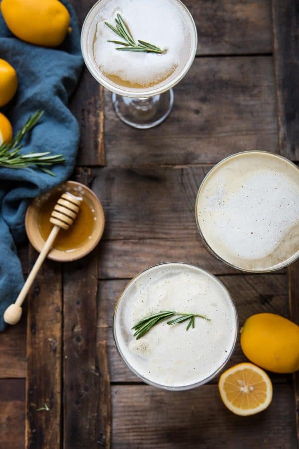 overhead view of three coupe glass cocktails with rosemary garnish and honey