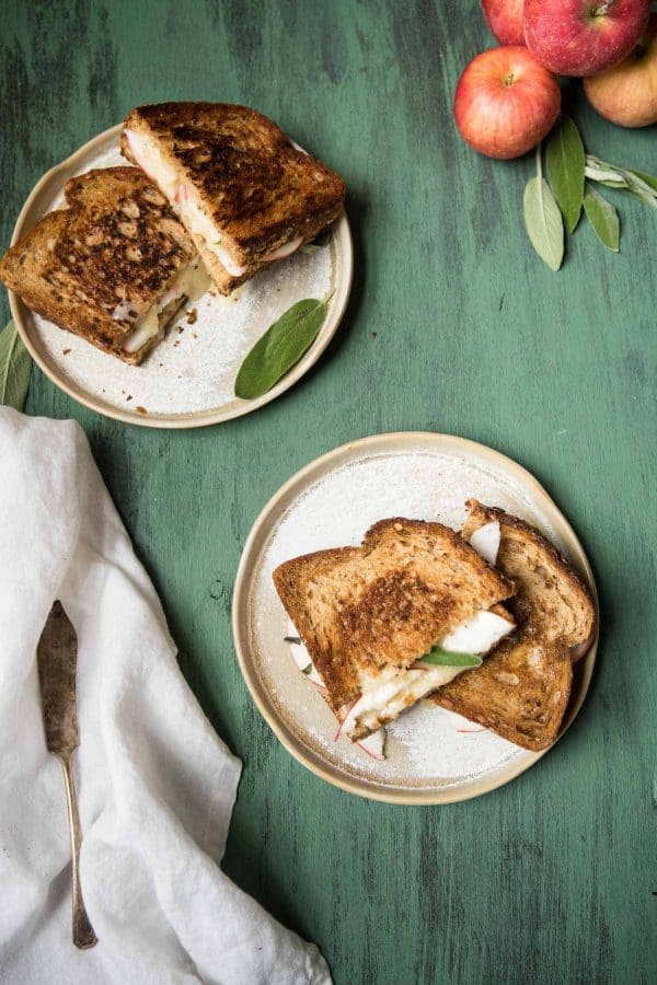 two grilled cheese sandwiches stacked on two plates with apples