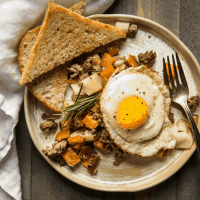 Fried egg over sweet potato hash with lamb and apples served with toast