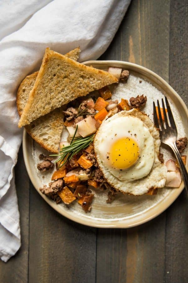 Fried egg over sweet potato hash with lamb and apples served with toast