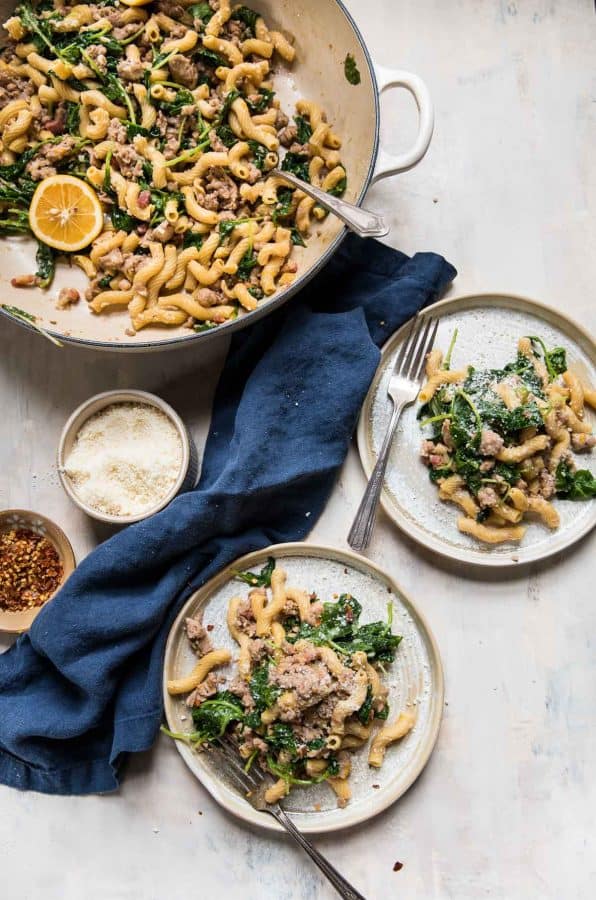 two plates of chickpea pasta with greens and sausage