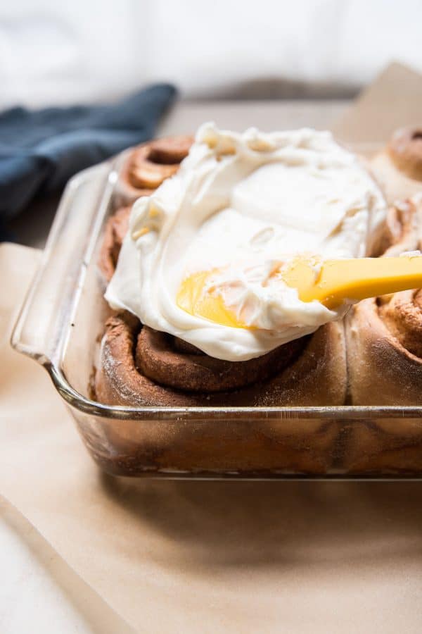 spreading frosting on cinnamon rolls in the pan