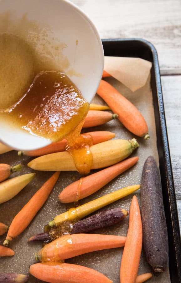 pouring honey and ginger mixture over carrots to be roasted