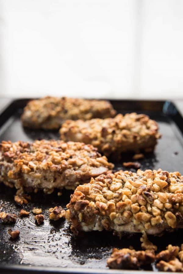 walnut coated pork chops on a black sheet tray after baking