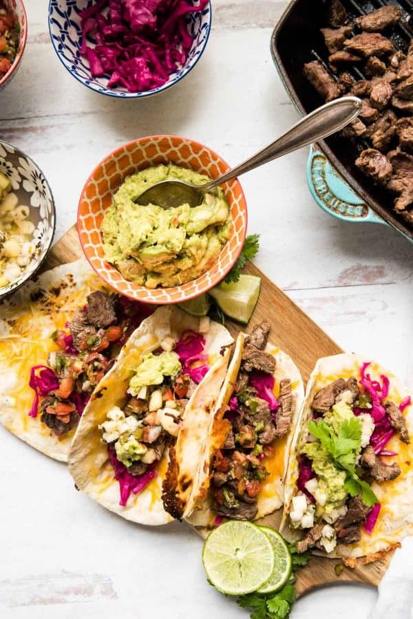 four tacos stacked on a wooden board with guac