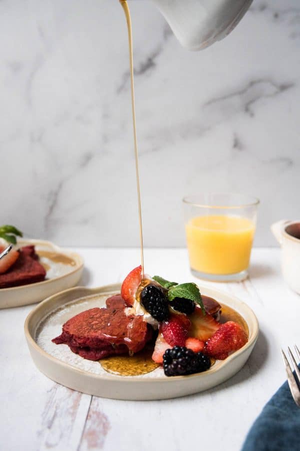 maple syrup pouring over a stack of red pancakes