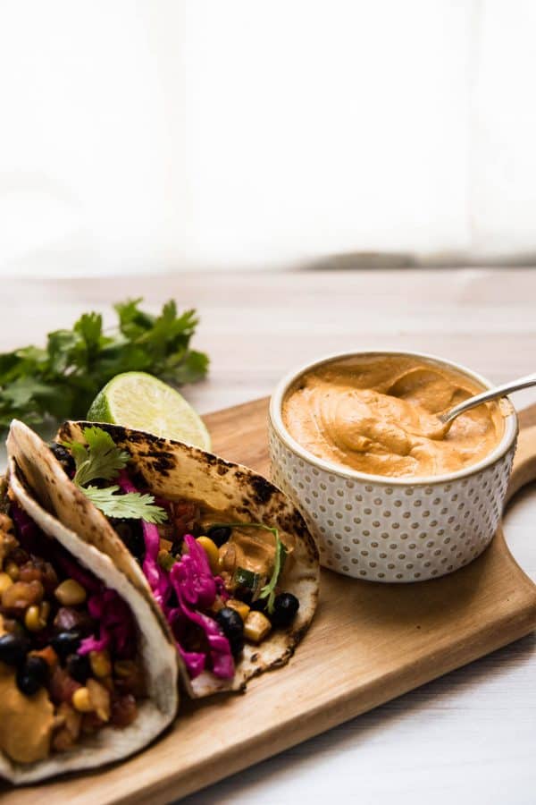 spoon in ramekin of chipotle aioli next to two tacos on a wooden board