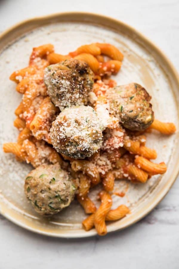 grated parmesan over turkey meatballs and red sauce pasta on a plate
