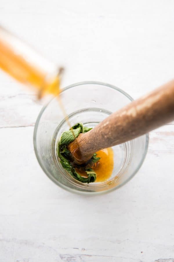 pouring maple syrup over mint in a glass