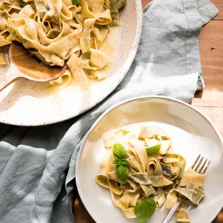 overhead close up of basil pappardelle wrapped around a fork and serving platter of pasta