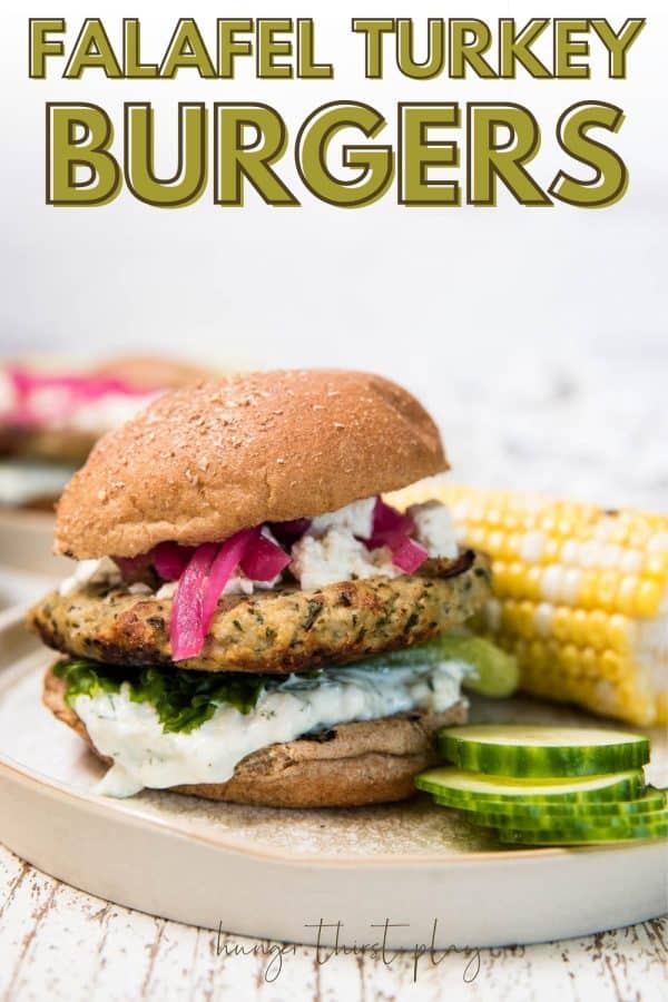 burger with toppings on bun with corn and cucumbers on plate