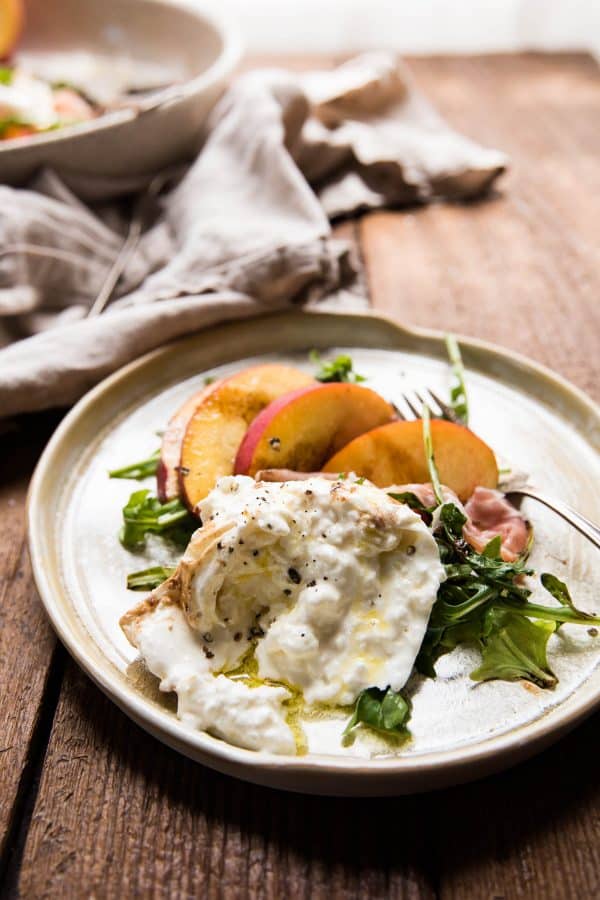 creamy torn burrata on a plate with peaches and arugula