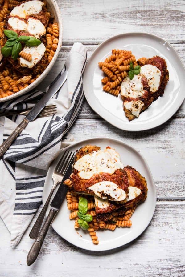 two servings of chicken parmesan over pasta on plates 