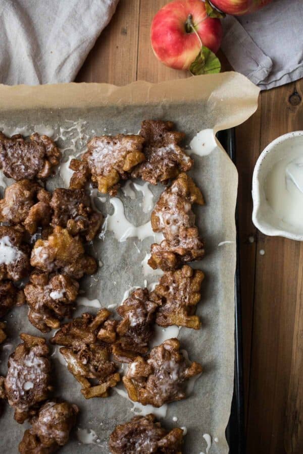 apple fritters on parchment paper with bowl of glaze