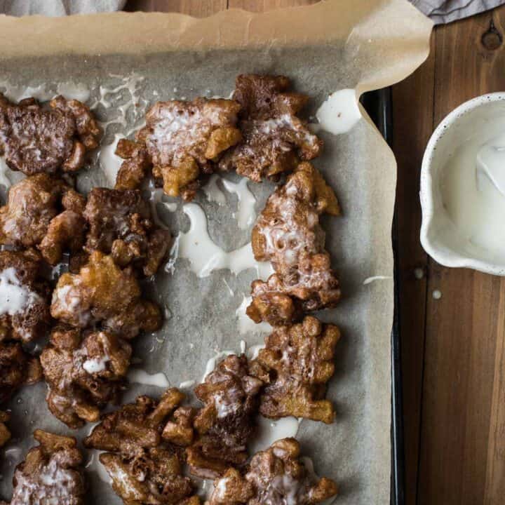 apple fritters on parchment paper with bowl of glaze