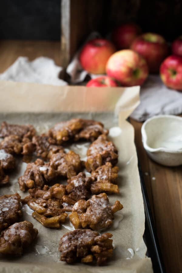 sourdough apple fritters on parchment with apples in the back