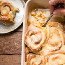 scooping a cinnamon roll out of a baking dish