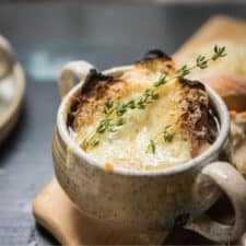 close up of broiled cheese and toast with fresh tyme sprig on a bowl of soup