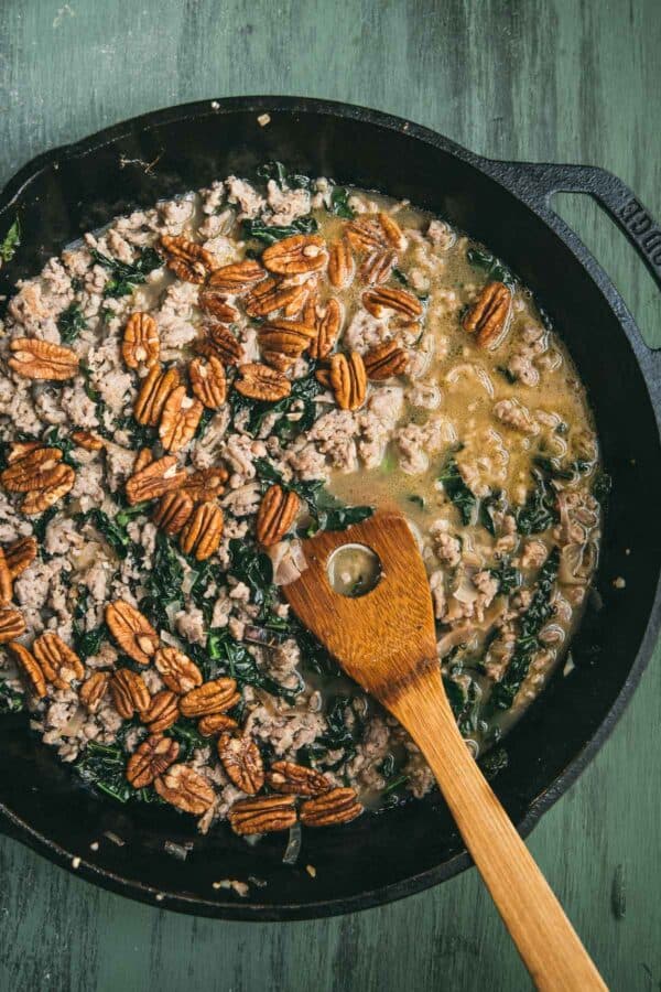 simmered sausage, kale, pecans and chicken stock in a skillet