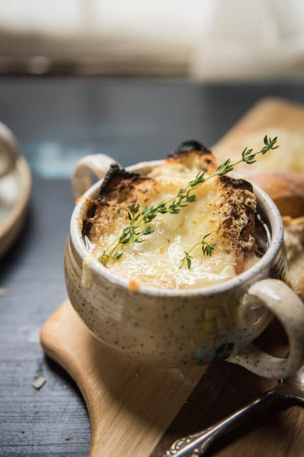 close up of broiled cheese and toast with fresh tyme sprig on a bowl of soup