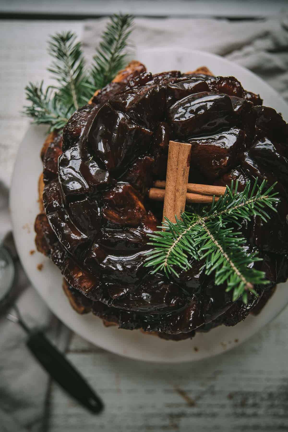 overhead of gooey monkey bread on a cake stand with cinnamon sticks and tree sprigs